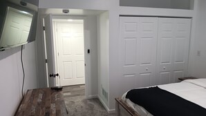 Quarto com piso de madeira, cama com cobertura preta, guarda-roupa branco e televisão na parede.
