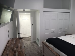 A bedroom with a wooden floor, a bed with a black cover, a white wardrobe, and a television mounted on the wall. - The Longview lake house (Coldwater)