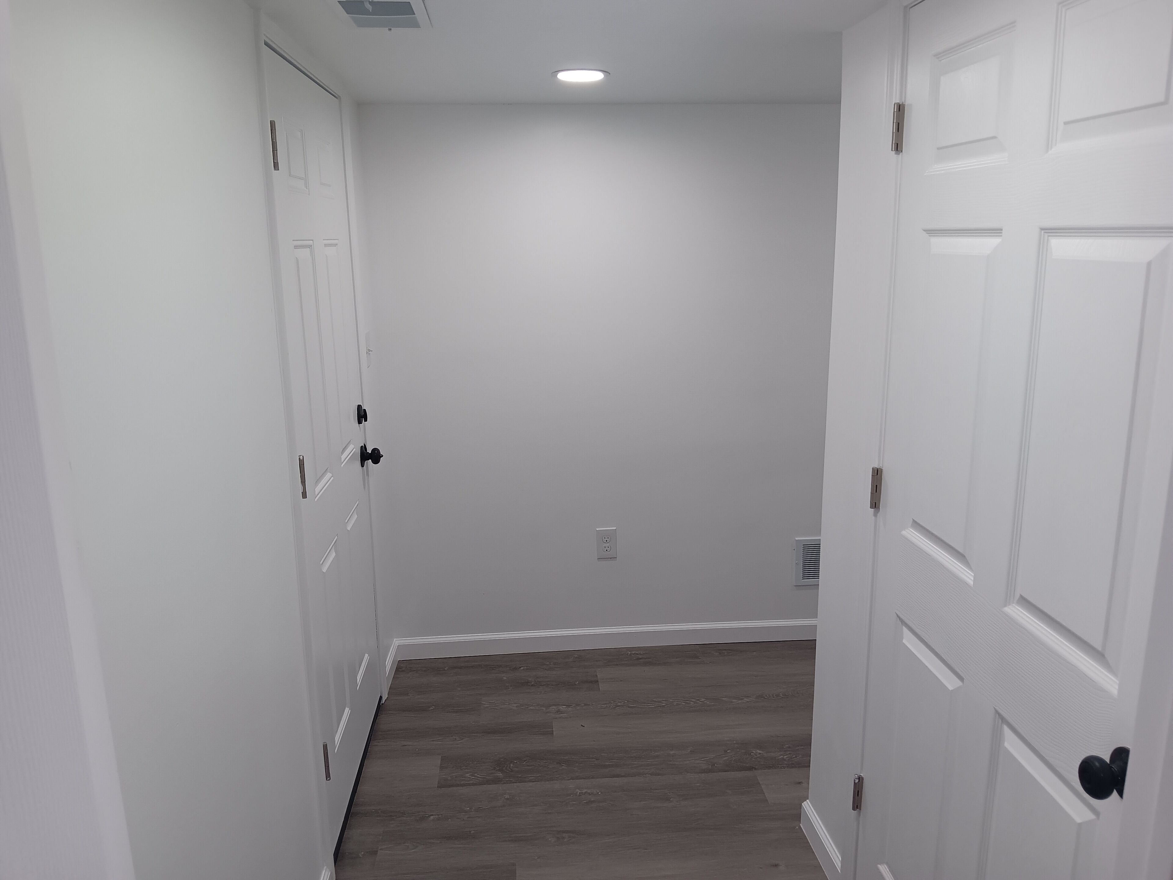 Un couloir aux murs blancs, au plancher en bois et aux portes blanches dotées de poignées noires.