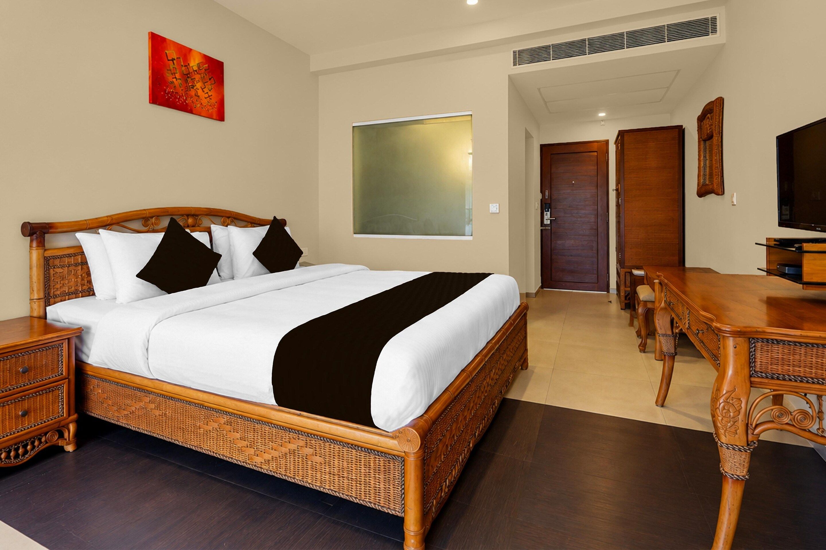 A hotel room with a large bed, a desk, a television, and a wall-mounted artwork.