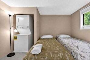 Una habitación pequeña con dos camas, una lavadora y una lámpara.