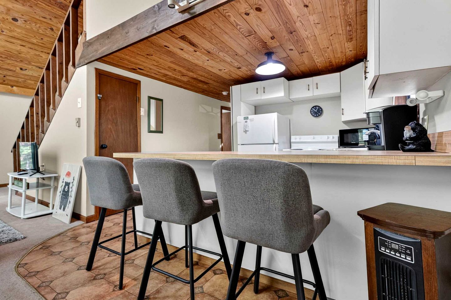 A kitchen with a wooden ceiling, a bar area with three chairs, and a refrigerator.