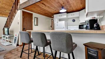 A kitchen with a wooden ceiling, a bar area with three chairs, and a refrigerator.