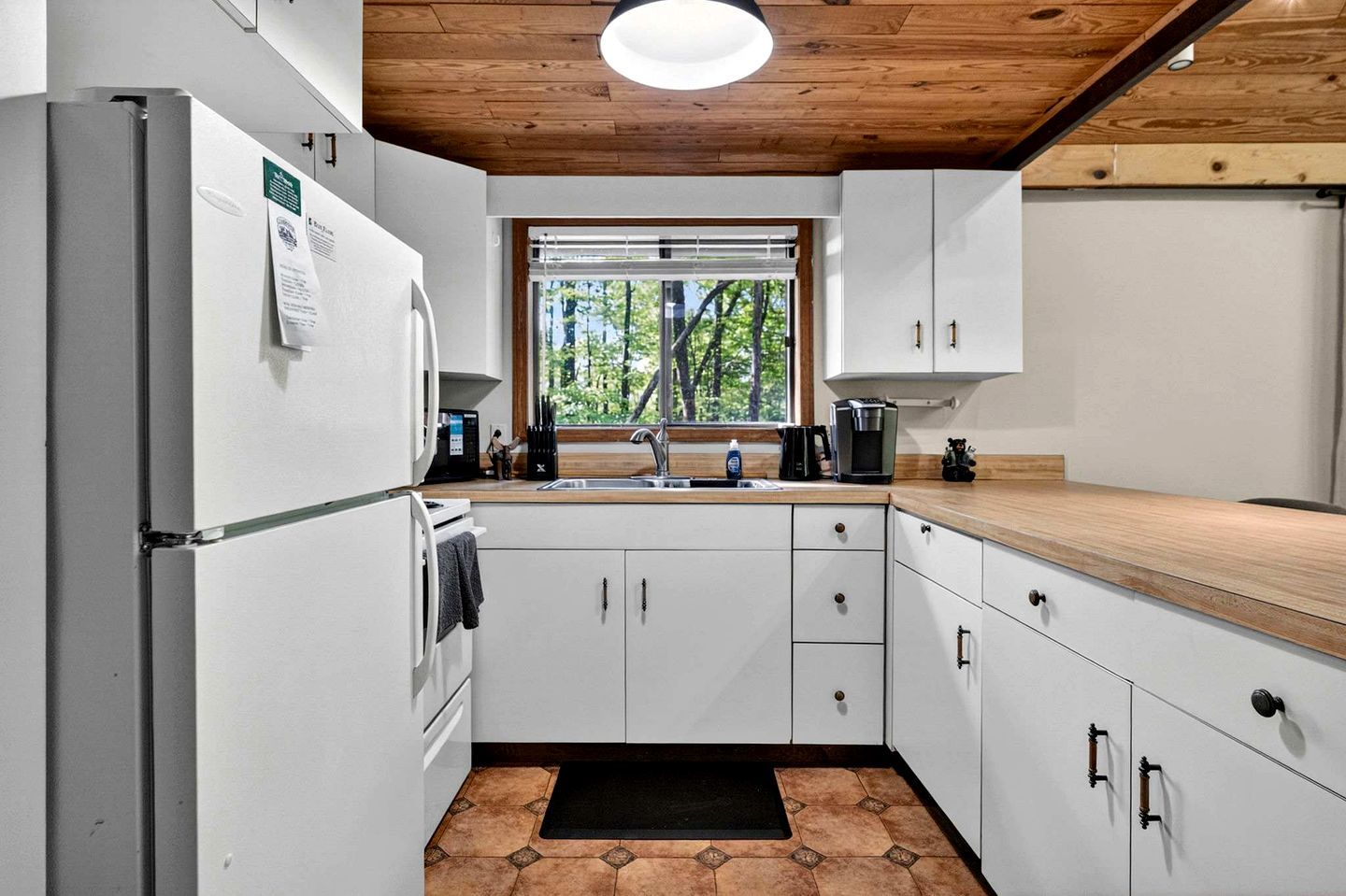 Une cuisine moderne avec des meubles blancs, un plan de travail en bois, un four encastré, un évier et une fenêtre donnant sur des arbres.