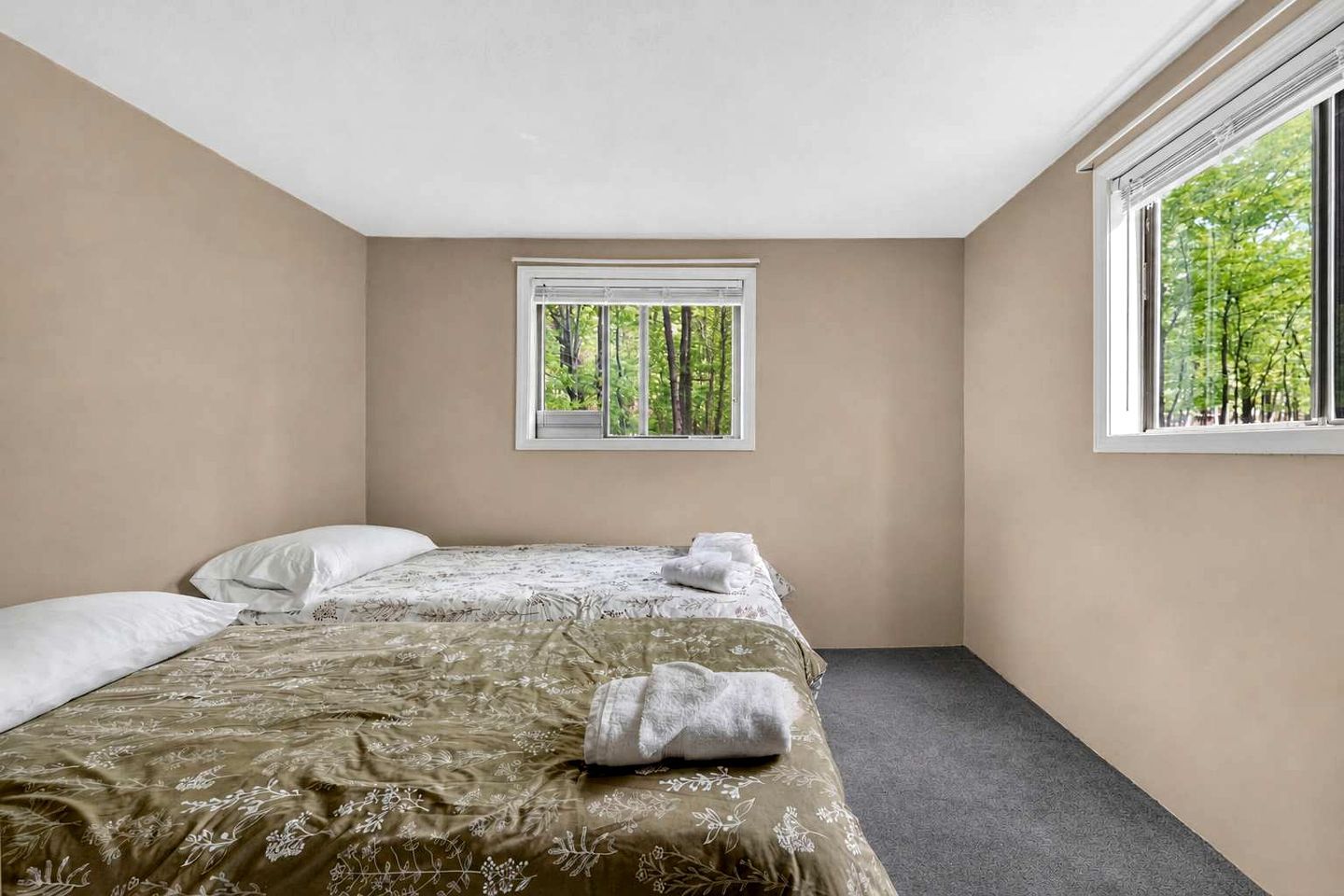Ein Schlafzimmer mit einem Bett, zwei Kissen, einem Fenster mit Blick auf Bäume und einem Teppichboden.