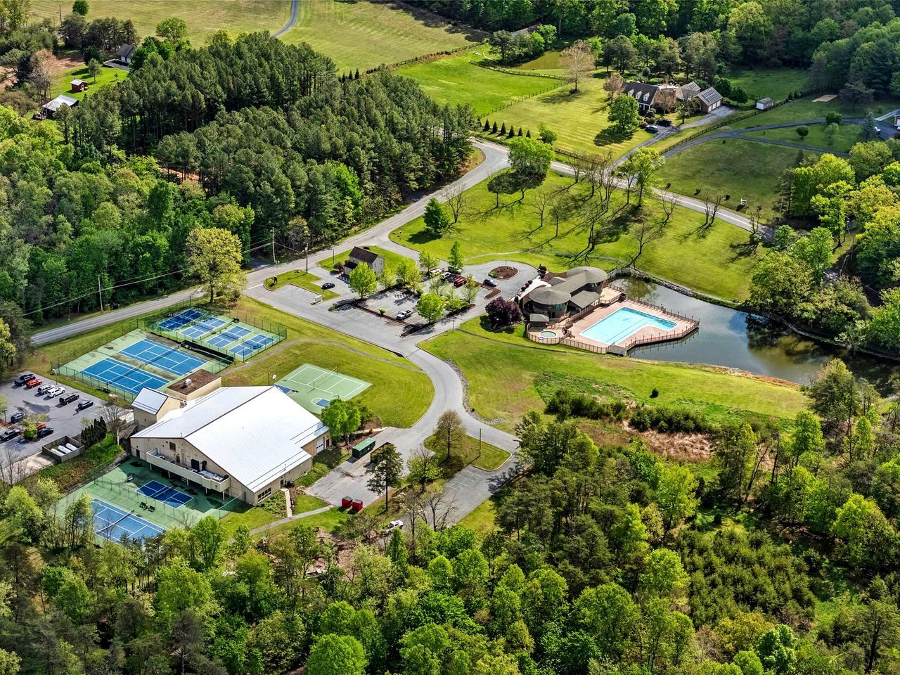 An aerial view of a residential area with multiple tennis courts, a swimming pool, and a large building with a flat roof.