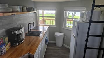 Una cocina compacta con encimera de madera, cafetera, microondas y cubo de basura.