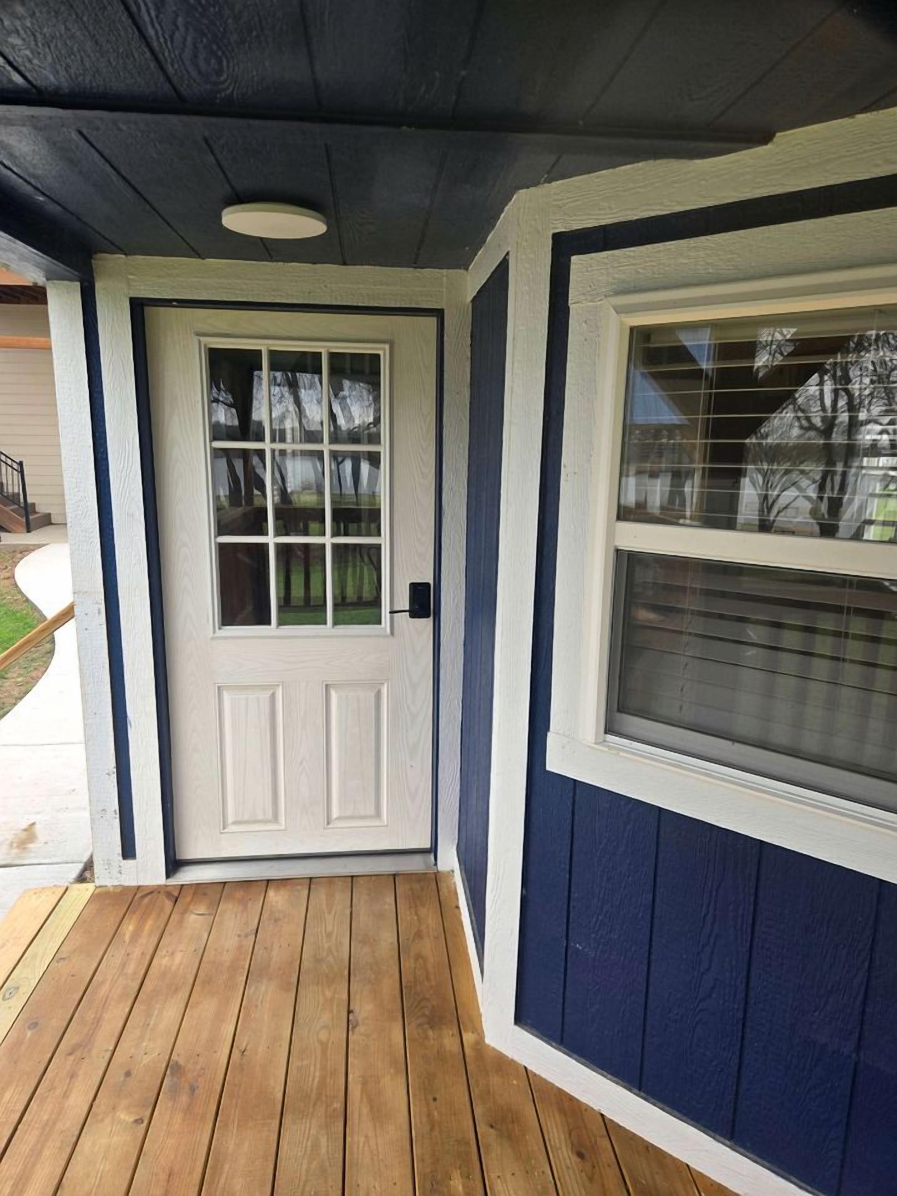 A wooden porch with a white door and a window with blinds.