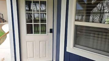 A wooden porch with a white door and a window with blinds.