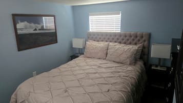 Un dormitorio con una cama, dos lámparas de noche, un ventanal con persianas y un cuadro en la pared.