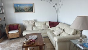 Un salon comprenant un canapé, un fauteuil en osier, une table basse, une lampe, un tableau et un lampadaire.