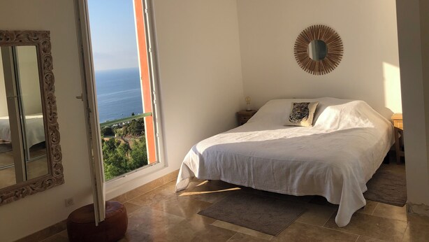 Une chambre avec un lit, un miroir, un élément de décoration murale rond et une vue sur la mer.