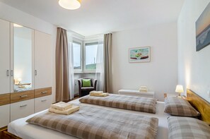 Ein Hotelzimmer mit zwei Betten, einem Sessel, einem Schreibtisch und einem Fenster mit Vorhängen.