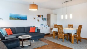 Una sala de estar moderna con un sofá, una mesa de centro, una mesa de comedor con sillas, una lámpara colgante y un cuadro en la pared.