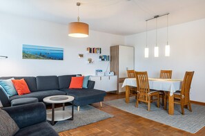 Ein modernes Wohnzimmer mit Sofa, Couchtisch, Esstisch mit Stühlen, einer Pendelleuchte und einem Bild an der Wand.