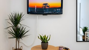 A modern living room with a flat-screen TV mounted on the wall, a round wooden table, two potted plants, a small side table with a remote control, and a patterned rug. - Aroma Holiday House with Wi-Fi and Air Conditioning (Rome)
