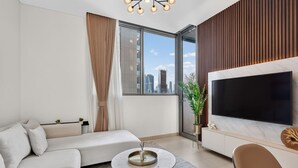 Ein modernes Wohnzimmer mit einer Couch, einem runden Couchtisch, einem Fernseher und Blick auf die Stadt.