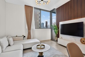 A modern living room with a sofa, a round coffee table, a TV, and a city view. - Your Urban Haven in Sobha Hartland (Dubai)