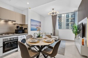 A modern kitchen with a dining area, a flat-screen TV, and a cityscape painting. - Your Urban Haven in Sobha Hartland (Dubai)