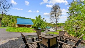 An outdoor seating area with a table and chairs, a building with a blue roof, and a grassy landscape. - Secluded Cabin Retreat with Hot Tub in Berkeley Springs, West Virginia (Berkeley Springs)