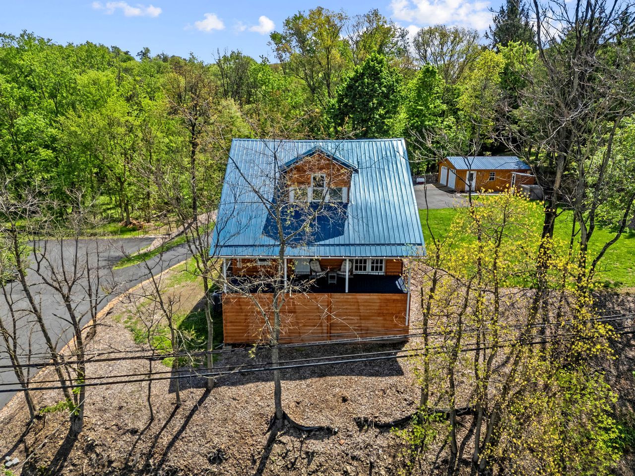 A small house with a blue roof, surrounded by trees and a dirt path.