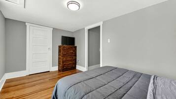Une chambre avec une commode en bois, une couvre-lit grise et une porte blanche.