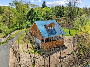 Une maison en bois avec un toit bleu, entourée d’arbres et bordée d’un chemin de terre.