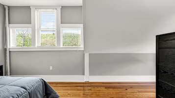 Una habitación con cama, ventana con persianas y suelo de madera.