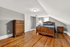Une chambre à coucher avec un lit en bois, une commode et une table de chevet, une porte blanche et une fenêtre.