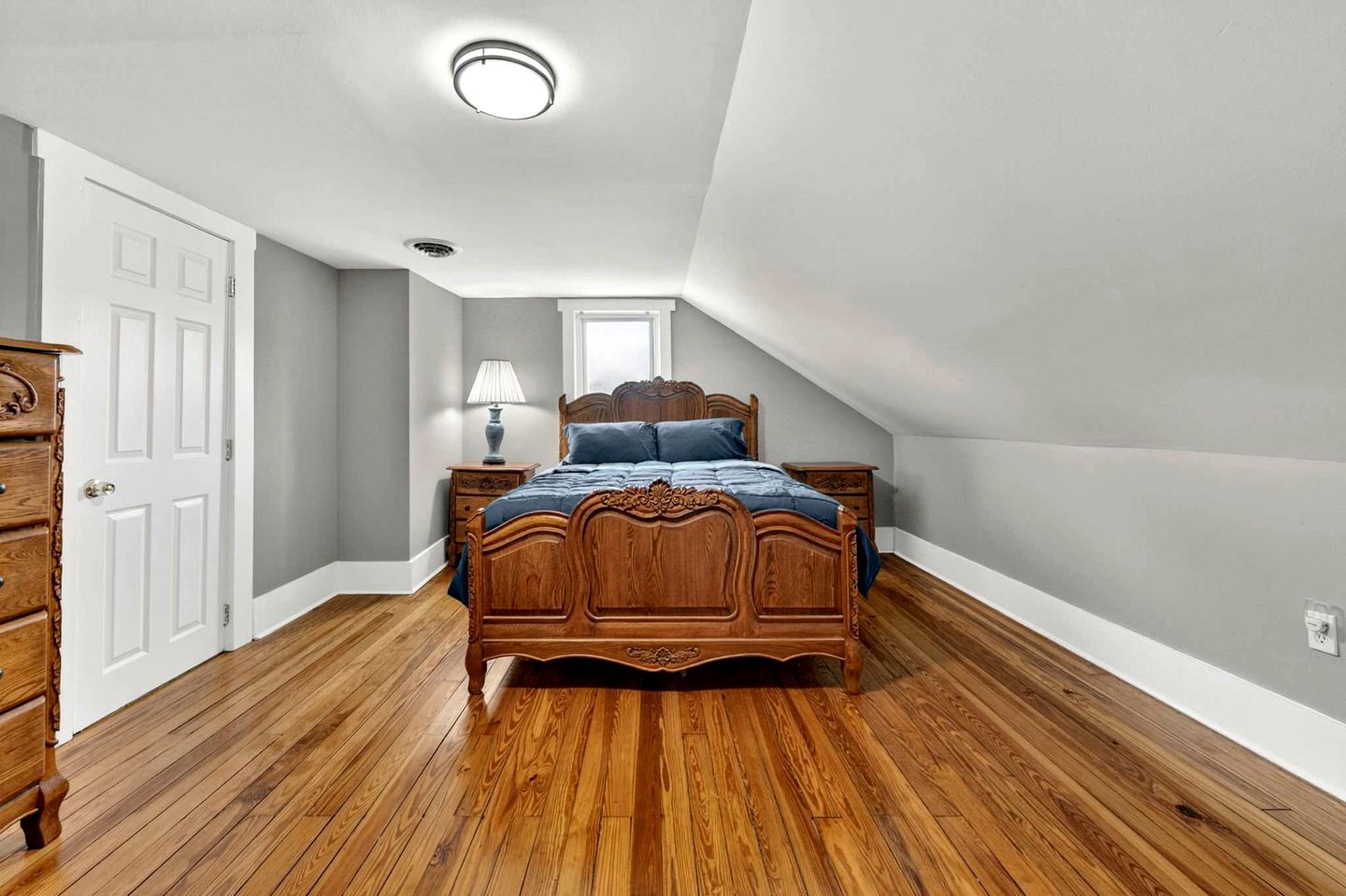 Un dormitorio con una cama de madera, una mesita de noche, un aparador y una lámpara en el techo.