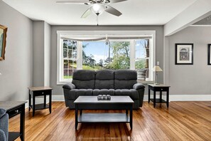 A living room with a sofa, coffee table, and a ceiling fan. - Secluded Cabin Retreat with Hot Tub in Berkeley Springs, West Virginia (Berkeley Springs)