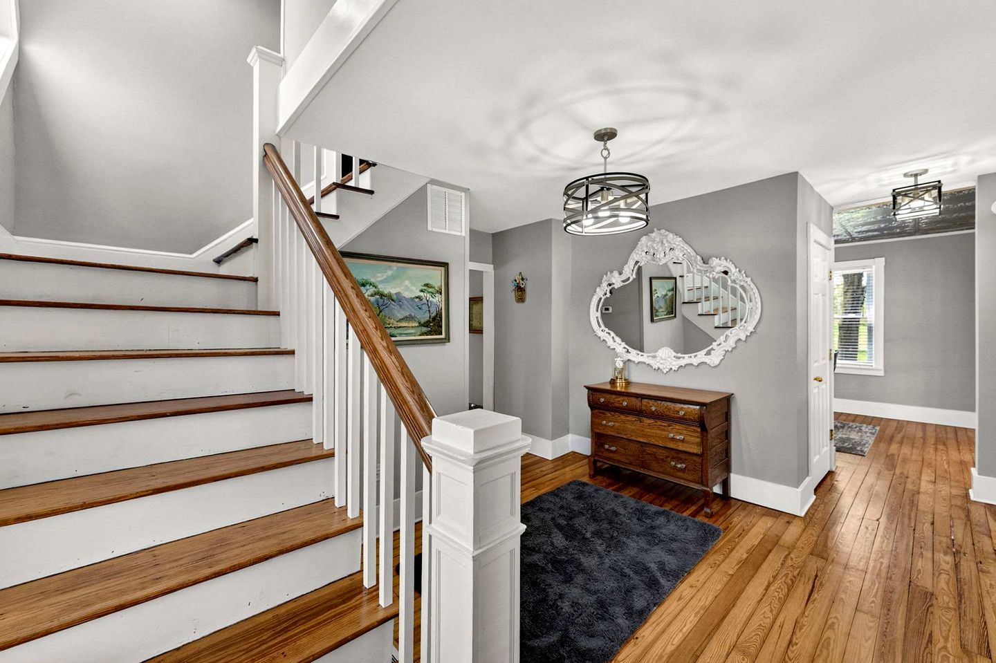 A staircase with wooden steps and white railings, a dark blue rug, a wooden dresser, and a large mirror on the wall.