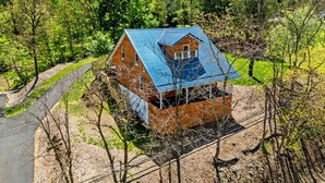 A wooden house with a blue roof surrounded by trees and a dirt path. - Secluded Cabin Retreat with Hot Tub in Berkeley Springs, West Virginia (Berkeley Springs)