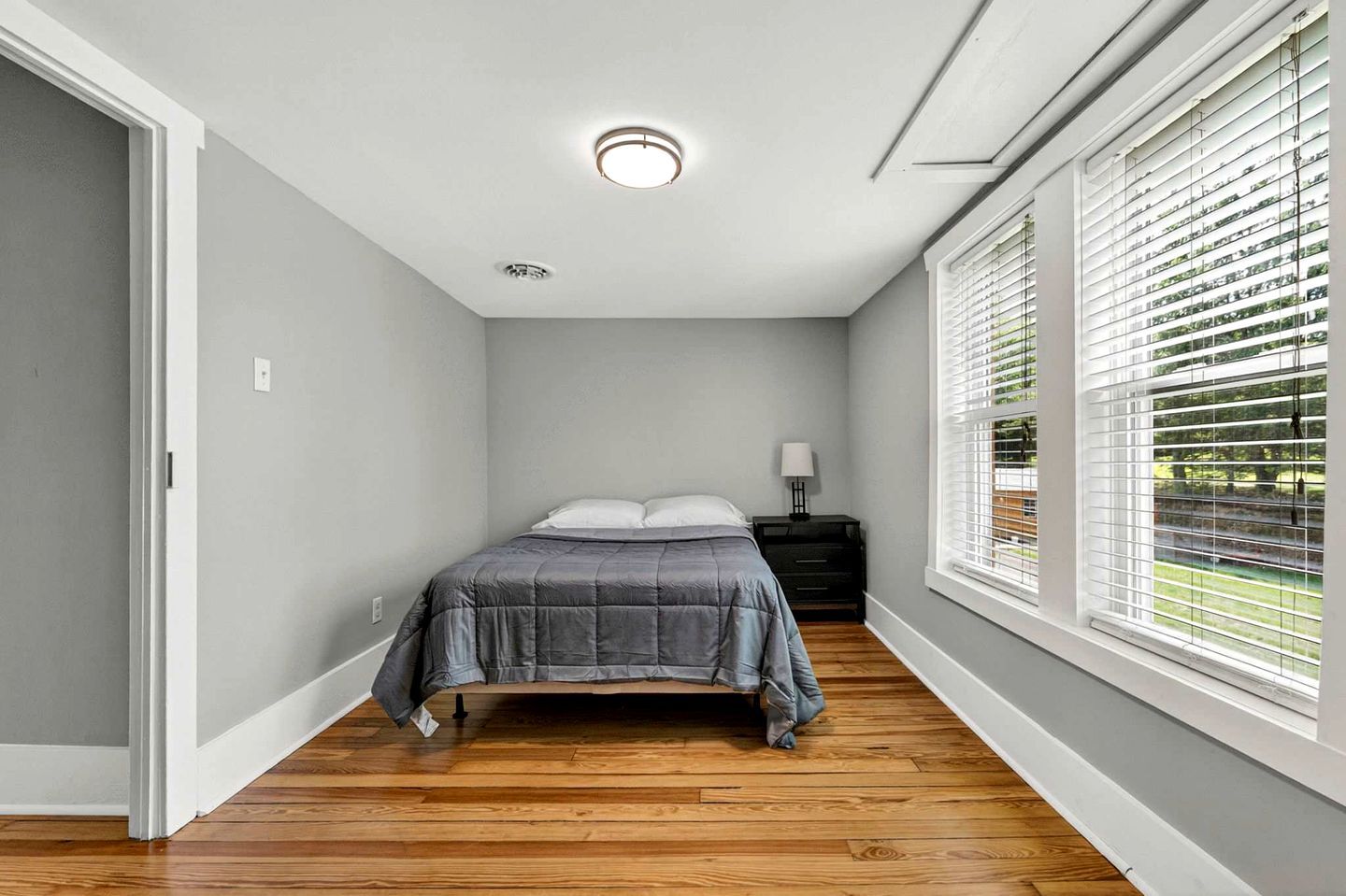 Une chambre à coucher avec un lit, une table de chevet, une lampe et une fenêtre avec des stores.