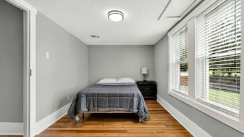 Une chambre à coucher avec un lit, une table de chevet, une lampe et une fenêtre avec des stores.