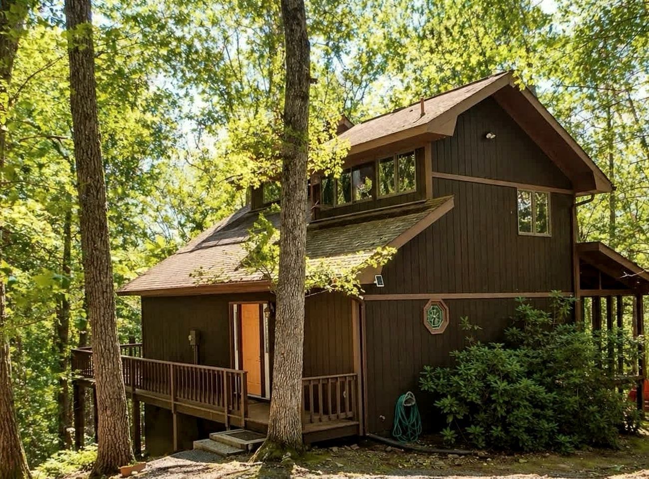 A two-story wooden cabin with a balcony, surrounded by trees.