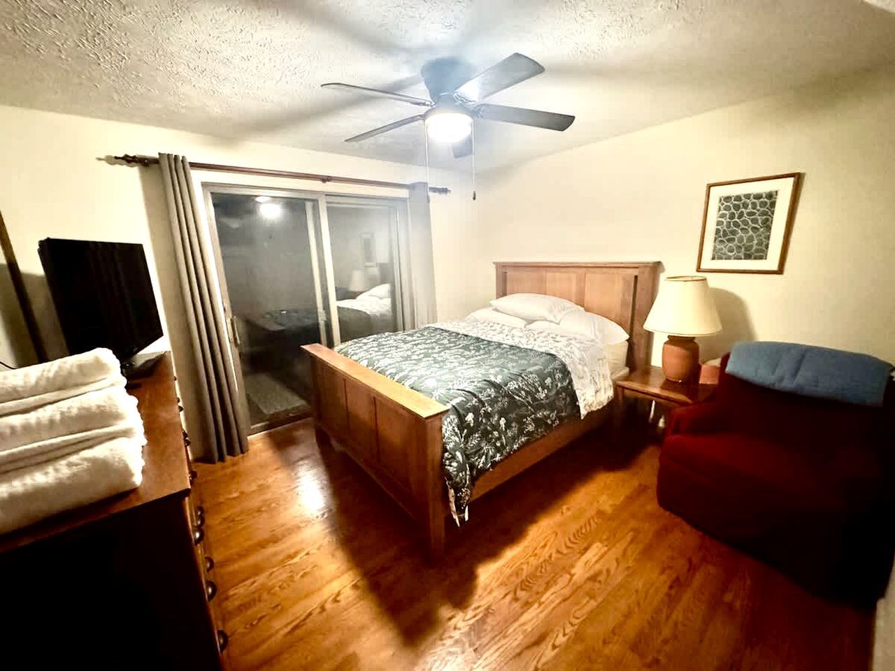 A bedroom with a bed, a nightstand, a chair, a ceiling fan, and a window with curtains.