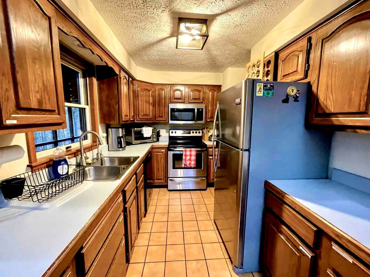 A compact kitchen with wooden cabinets, a stainless steel refrigerator, a microwave, an oven, and a sink.