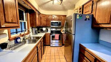 A compact kitchen with wooden cabinets, a stainless steel refrigerator, a microwave, an oven, and a sink.