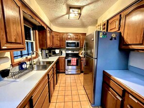 A compact kitchen with wooden cabinets, a stainless steel refrigerator, a microwave, an oven, and a sink.