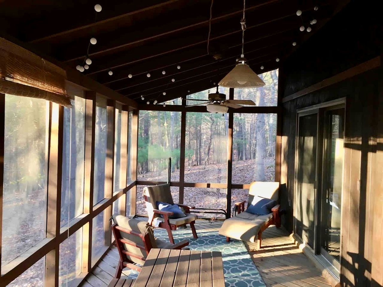 A wooden deck with seating and a ceiling fan, overlooking a forested area.