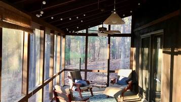 A wooden deck with seating and a ceiling fan, overlooking a forested area.