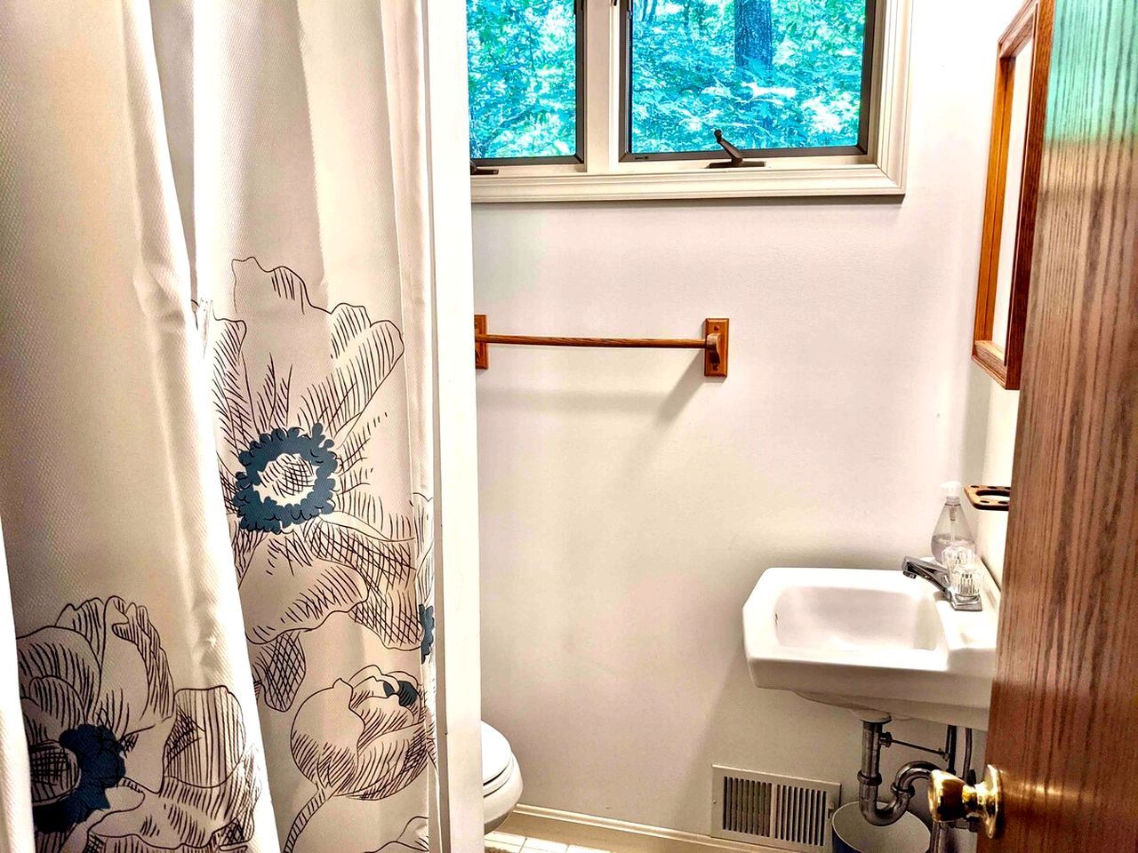 A bathroom with a shower curtain, a window with a view of trees, a sink, and a towel rack.