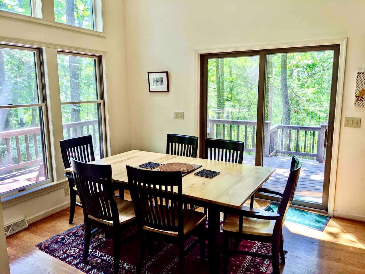 A dining area with a wooden table and chairs, large windows, and a view of trees.