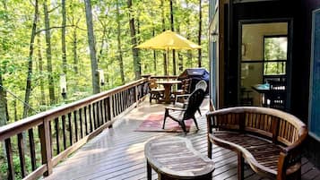 Un terrazza in legno con mobili da esterno, un tavolo e sedie, affacciata su una zona boschiva.