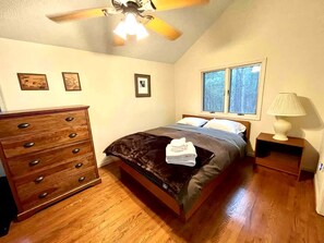 A bedroom with a bed, dresser, nightstand, lamp, and ceiling fan.