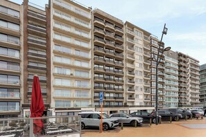 Ein mehrstöckiges Wohnhaus mit Balkonen, ein Parkplatz mit Autos und ein roter Regenschirm.