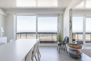 Eine moderne Küche mit einem großen weißen Tisch, zwei Stühlen und Meerblick durch große Fenster.