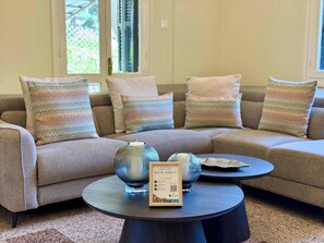 Uma sala de estar moderna com um sofá bege, almofadas listradas e uma mesa de centro redonda com vasos decorativos e um livro emoldurado.