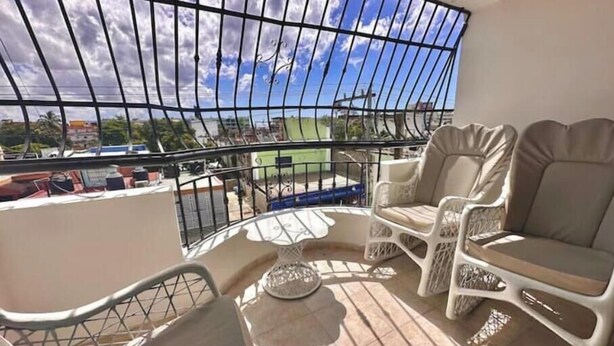 Ein Balkon mit Metallgeländer, zwei weiß gepolsterte Stühle, ein kleiner runder Tisch und Blick auf die Stadtlandschaft.